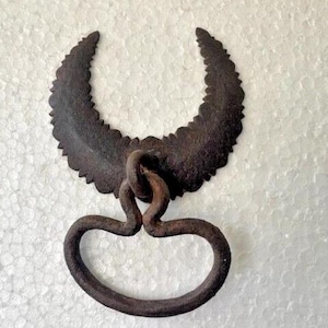 May include: A rustic, antique-style metal door pull with a crescent-shaped top and a looped handle. The metal has a dark, aged finish, suggesting it's an older piece. The design is simple yet decorative, suitable for vintage or farmhouse decor.