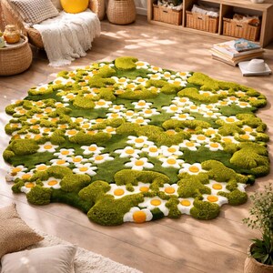 May include: A green rug with a daisy flower design. The rug features white petals with yellow centers, set against a green background. The rug is placed on a wooden floor, with other home decor items in the background.