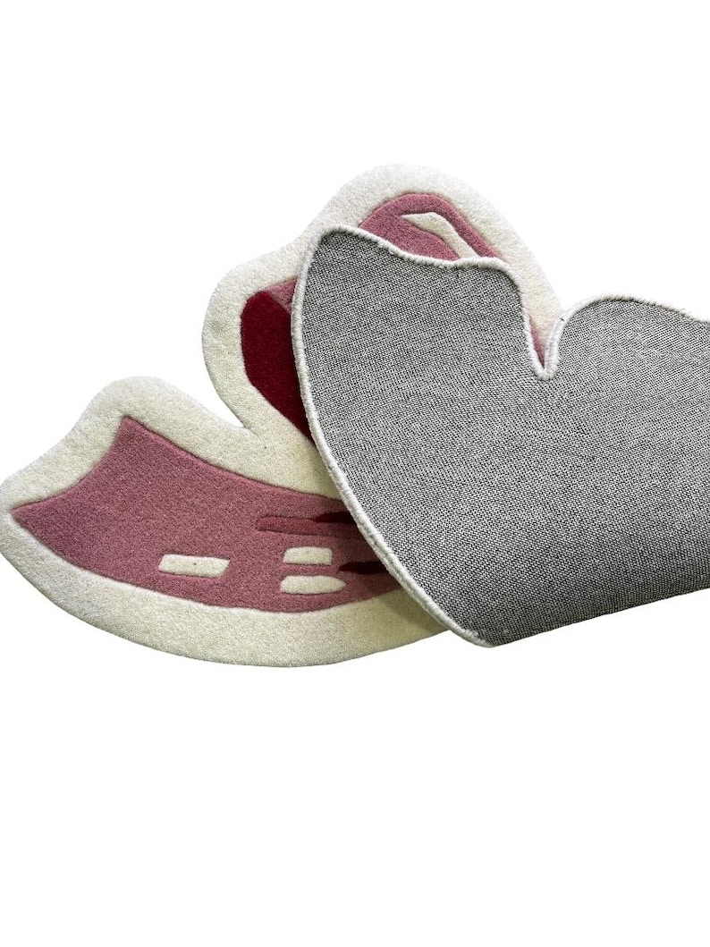 May include: Two heart-shaped rugs. One rug is pink with white and red accents. The other rug is gray. The rugs are made of a soft, textured material. The rugs are designed to be decorative.