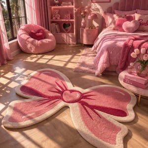May include: A pink bedroom with a large bow-shaped rug. The rug is light pink with a darker pink outline and a heart in the center. The room has a pink bed, a beanbag chair, and a bookshelf with a "Barbie" sign.
