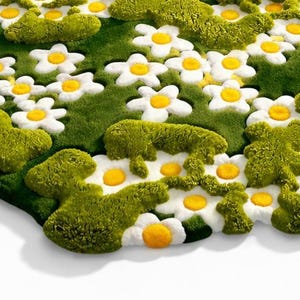 May include: A whimsical rug featuring a design of white daisies with yellow centers and green foliage. The rug has a unique, organic shape and is set against a white background. The rug's dimensions are not visible.