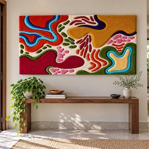 Pode incluir: Uma grande tapeçaria retangular de parede com uma textura tufada de pelo alto e um design abstrato de formas orgânicas e fluidas em cores vibrantes, incluindo vermelho, laranja, amarelo, rosa, verde, azul e creme sobre um fundo branco.