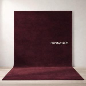 May include: A large, rectangular burgundy rug with a soft, velvety texture. The rug is displayed against a white wall, with the text "YourRugHaven" in the center. The rug's color is a deep, rich shade of red.