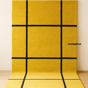 May include: A saffron yellow rug with a bold black grid pattern. The rug is rectangular and has a soft, textured appearance. The text "Your Rug Haven" and "Saffron Yellow" are visible.