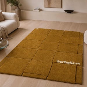 May include: Mustard yellow geometric rug with a textured surface. The rug is composed of rectangular and square shapes, creating a modern design. The rug is placed on a light-colored wooden floor in a living room setting.