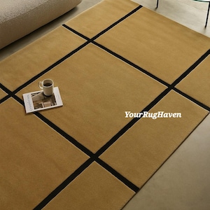 May include: A mustard-colored rectangular rug with a geometric black grid pattern. A white mug with coffee and a magazine are on the rug. The text "YourRugHaven" is visible on the rug.
