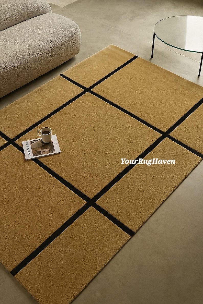 May include: A mustard-colored rectangular rug with a geometric black grid pattern. A white mug with coffee and a magazine are on the rug. The text "YourRugHaven" is visible on the rug.