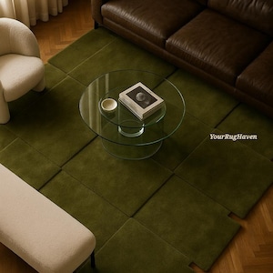 May include: An overhead shot of a living room with a green rug, brown leather sofa, and glass coffee table. A white chair and bench are also visible. The rug is made of square sections. The coffee table has a book and a small bowl.