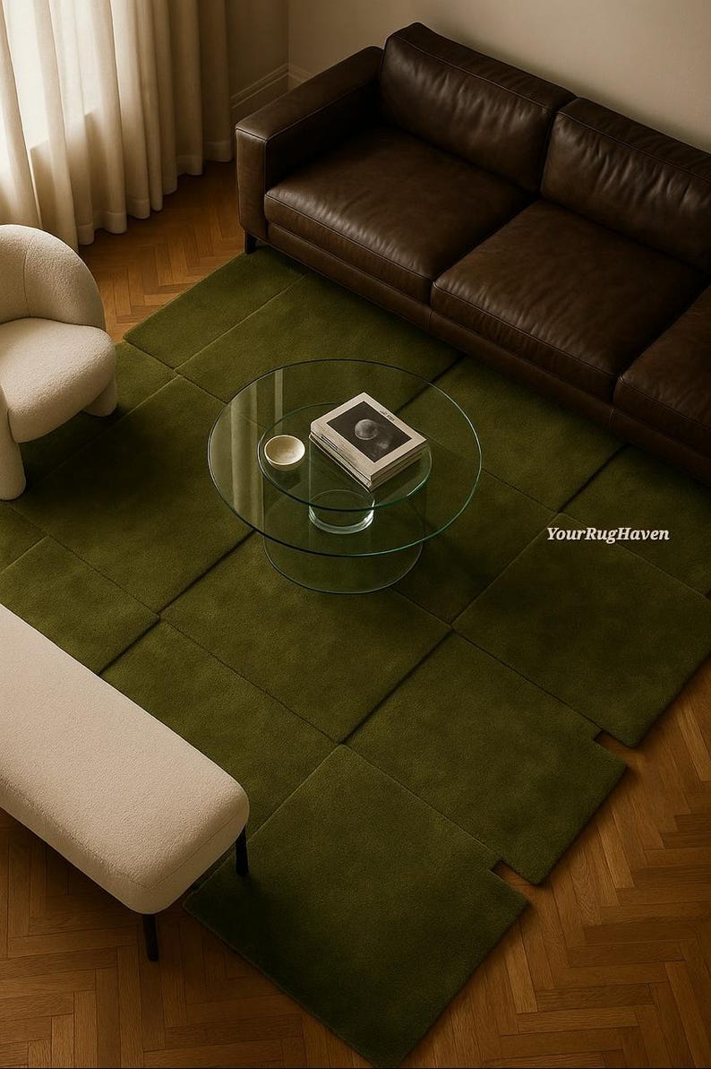 May include: An overhead shot of a living room with a green rug, brown leather sofa, and glass coffee table. A white chair and bench are also visible. The rug is made of square sections. The coffee table has a book and a small bowl.