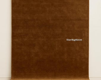 May include: A rectangular area rug in a solid, deep brown colour with a soft, textured pile surface. The text "YourRugHaven" is printed in white on the right side of the rug. The rug is positioned vertically against a plain, light-coloured wall.