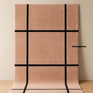 May include: A rectangular rug in a warm blush color with a black grid pattern. The rug is displayed on a wooden floor, with the text "Your Rug Haven" and "Warm Blush" visible.