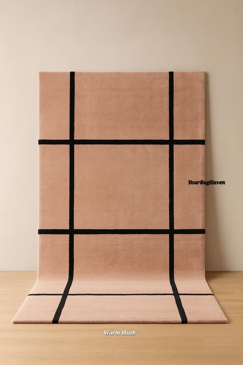 May include: A rectangular rug in a warm blush color with a black grid pattern. The rug is displayed on a wooden floor, with the text "Your Rug Haven" and "Warm Blush" visible.