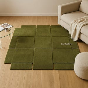 May include: A modular olive green rug composed of multiple square and rectangular pieces. The rug is arranged in a geometric pattern on a light wood floor, with a beige sofa and a small glass table in the background. The text "YourRugHaven" is visible.