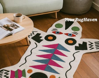 May include: A cream-colored, abstract rug with a whimsical design. The rug features geometric shapes in pink, blue, green, orange, and black. The rug is shaped like a stylized animal and is placed on a hardwood floor.