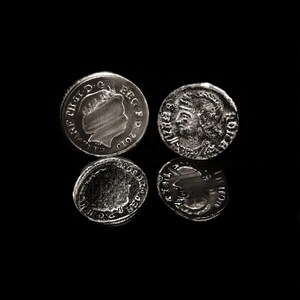 May include: Four silver coins are displayed against a black background. Two coins are visible, with the other two reflected below. One coin features a profile, the other has a detailed bust. The coins appear to be historical.