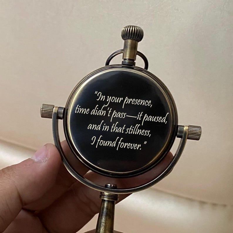 May include: A vintage-style, brass-colored compass with a black face. The compass features the quote, "In your presence, time didn't pass&mdash;it paused, and in that stillness, I found forever." The compass has a decorative top and side handles.