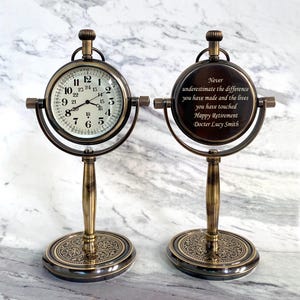 May include: Two antique-style desk clocks with a bronze finish. One clock displays the time, while the other features an engraved message: "Never underestimate the difference you have made and the lives you have touched Happy Retirement Docter Lucy Smith."