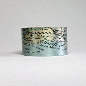 May include: A cylindrical bracelet with a map design. The map features place names like Amalfi, Positano, and Praiano. The bracelet is light blue with a vintage aesthetic. The text on the bracelet includes the number 813.