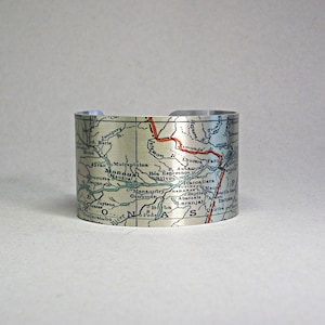 May include: A silver metal cuff bracelet with a vintage map of the Amazon River region of Brazil. The map is printed in shades of blue, green, and red, with the names of towns and cities printed in black.