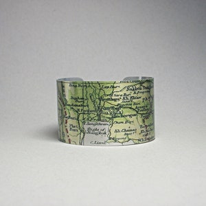 May include: A silver cuff bracelet featuring a vintage map design with green and red accents. The map includes place names like Bangkok and Lop Buri. The bracelet is a wide, open-ended style.