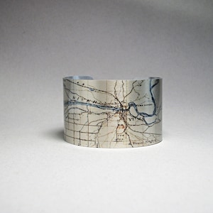 May include: A silver metal cuff bracelet with a vintage map of Yuma, Arizona printed on it. The map shows the Yuma River, Yuma School, and Yuma Heights.