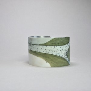 May include: A silver cuff bracelet with a green and white map design. The map shows a river or waterway with a small town or village.