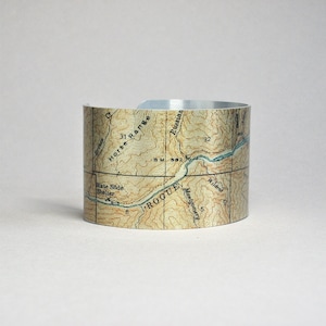 May include: A silver metal cuff bracelet with a vintage map design. The map shows a portion of the Rogue River in Oregon, with the Horse Range, the Rogue River, and the towns of Montgomery and Wildcat.