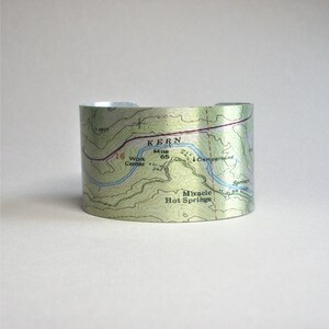 May include: A silver metal cuff bracelet with a topographic map design. The map shows the Kern River and Miracle Hot Springs in California. The text "Mile 65" is visible on the map.