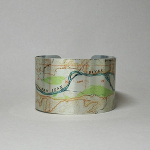 May include: A silver metal cuff bracelet with a vintage map design. The map features a river labeled "San Juan River" and "4300" in the center. The map is printed on a silver metal cuff bracelet.