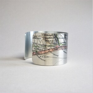May include: A silver metal cuff bracelet featuring a vintage map of the South Coast of England. The map shows the towns of Worthing, Shoreham, Lancing, Sompting, and Littlehampton.