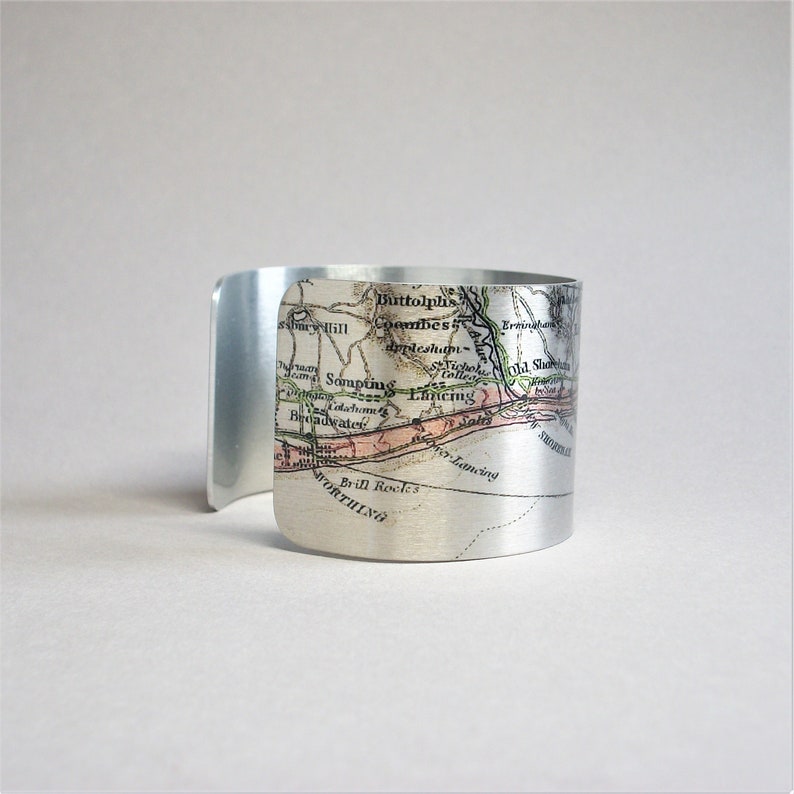 May include: A silver metal cuff bracelet featuring a vintage map of the South Coast of England. The map shows the towns of Worthing, Shoreham, Lancing, Sompting, and Littlehampton.