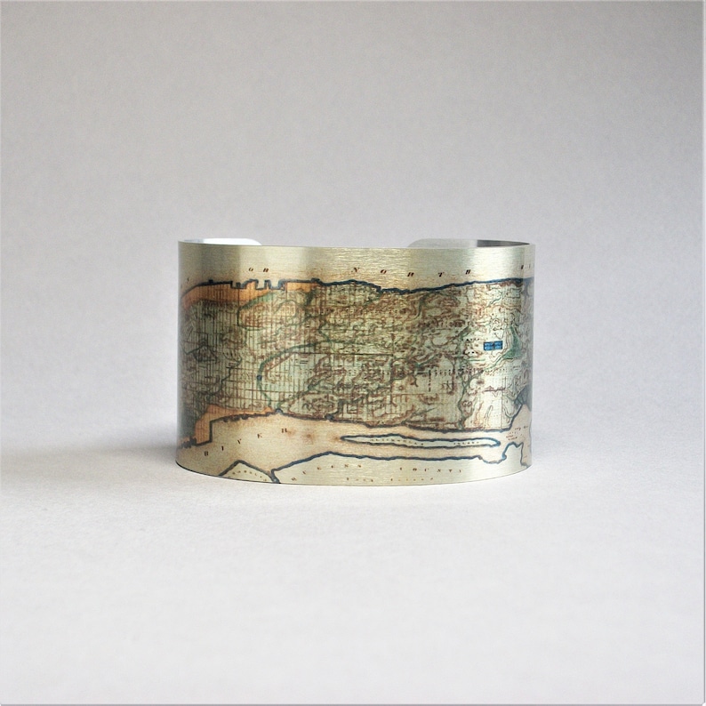 May include: A silver cuff bracelet with a vintage map of an island printed on it. The map is in shades of brown, green, and blue.