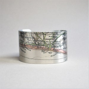 May include: A silver metal cuff bracelet featuring a vintage map of Brighton, England printed on it. The map shows the location of Brighton, Portslade, and surrounding areas. The map is in shades of green, brown, and pink.