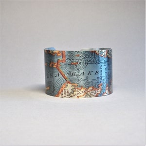 May include: A silver metal cuff bracelet with a vintage map of Chesapeake Bay printed on it. The map is in shades of blue, brown, and white. The text on the map includes "Chesapeake Bay", "Maryland", "Virginia", and "Delaware".