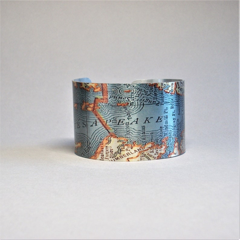 May include: A silver metal cuff bracelet with a vintage map of Chesapeake Bay printed on it. The map is in shades of blue, brown, and white. The text on the map includes "Chesapeake Bay", "Maryland", "Virginia", and "Delaware".