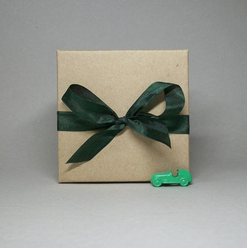 May include: A brown gift box with a green satin ribbon tied in a bow. A small green toy car is in front of the box.