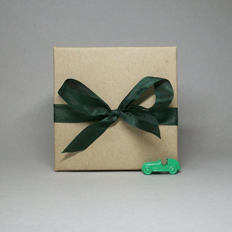 May include: A brown cardboard gift box with a green satin ribbon tied in a bow. A small green toy car is in front of the box.