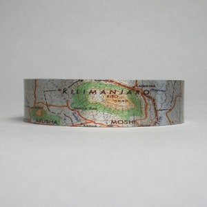 May include: A silver metallic tape with a map of Mount Kilimanjaro printed on it. The map shows the location of the summit, Kibo, and the surrounding towns of Moshi and Arusha.