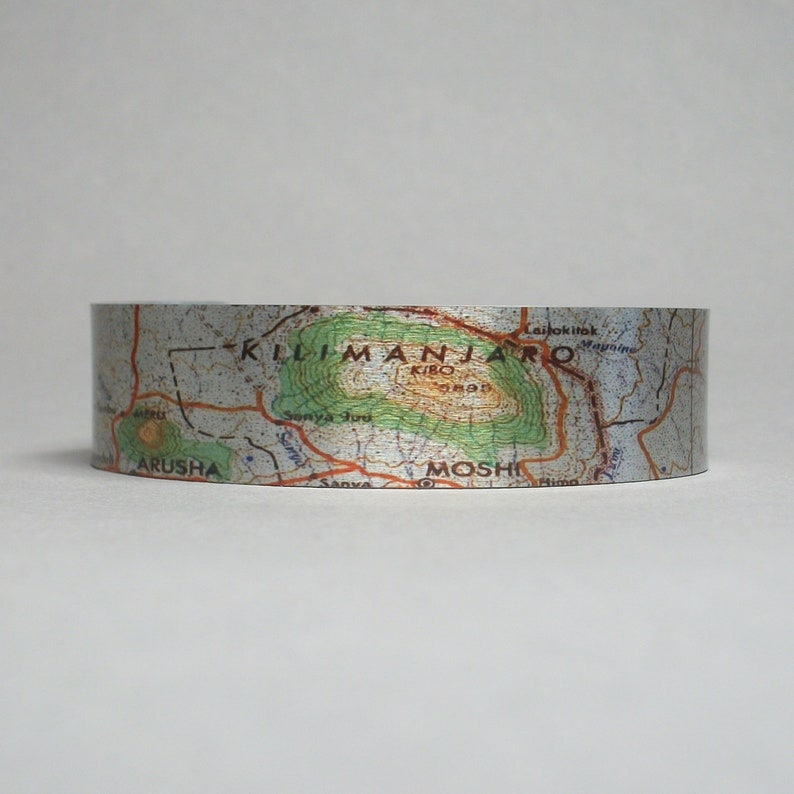 May include: A silver metallic tape with a map of Mount Kilimanjaro printed on it. The map shows the location of the summit, Kibo, and the surrounding towns of Moshi and Arusha.