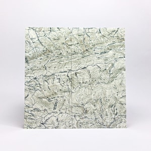 May include: A square topographic map print featuring detailed contour lines, elevation markings, and geographical labels in black ink on a cream-colored background. The map displays complex terrain, mountain ridges, and valleys with text.