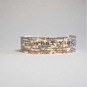 May include: A silver metal cuff bracelet with a vintage map of West Virginia printed on it. The map shows the cities of Morgantown, Clarksburg, Fairmont, Grafton, and Kingwood.