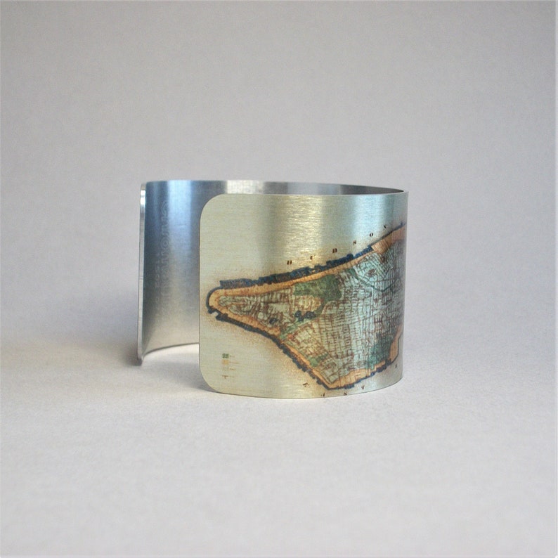 May include: A silver metal cuff bracelet with a printed image of a map of an island. The map is in shades of brown, green, and blue.
