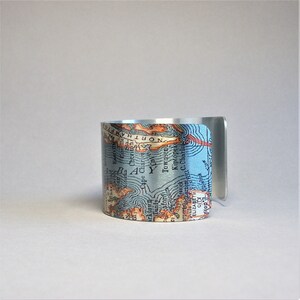 May include: A silver cuff bracelet with a vintage map design featuring the text "NORTHAMPTON" and "Cape Charles".