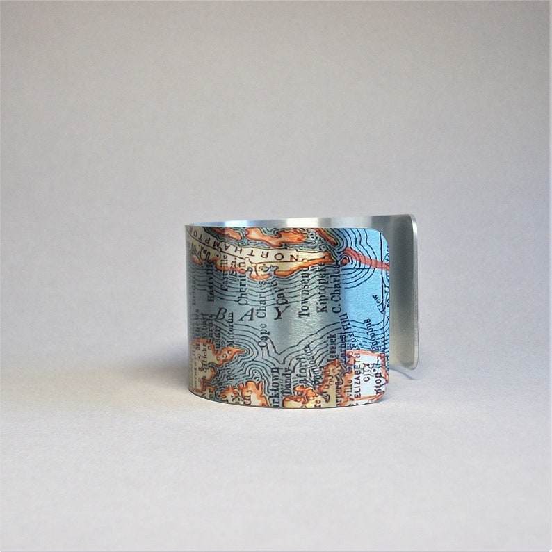 May include: A silver cuff bracelet with a vintage map design featuring the text "NORTHAMPTON" and "Cape Charles".