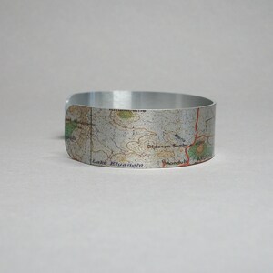 May include: A silver metal bracelet with a map of a region in Tanzania printed on it. The map shows the names of locations like Lake Manyara, Oldonyo Sambu, and Mondul.