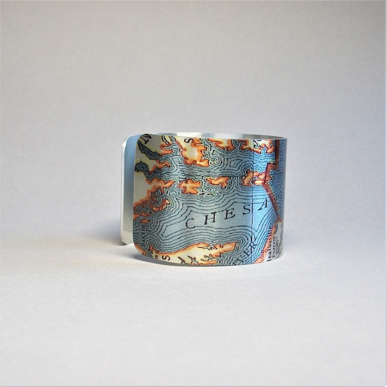May include: A silver cuff bracelet with a map of the Chesapeake Bay printed on it. The map is in shades of blue, green, and orange.