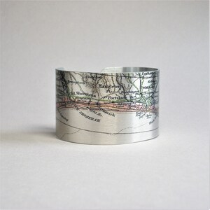 May include: A silver metal cuff bracelet featuring a vintage map of the area around Shorneham, England. The map is printed in black, green, and pink on the silver metal.