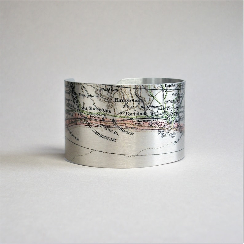 May include: A silver metal cuff bracelet featuring a vintage map of the area around Shorneham, England. The map is printed in black, green, and pink on the silver metal.