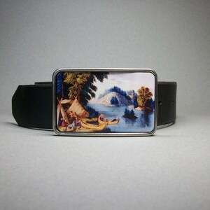 May include: A silver belt buckle with a colorful image of a lake scene with trees, a tent, and canoes. The buckle is attached to a black leather belt.