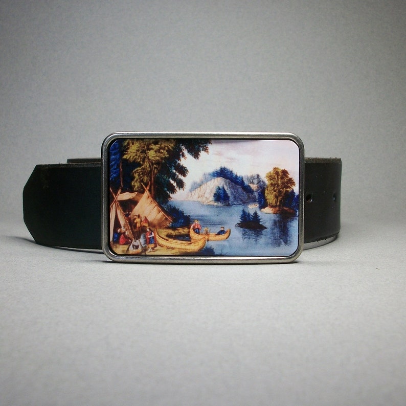 May include: A silver belt buckle with a colorful image of a lake scene with trees, a tent, and canoes. The buckle is attached to a black leather belt.